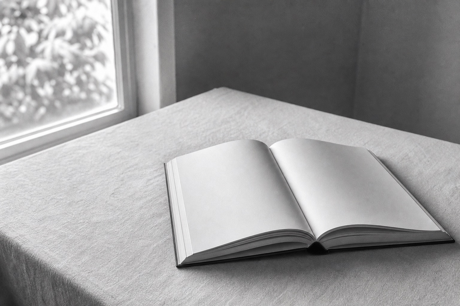 An open blank book resting on linen beside a softly lit window.