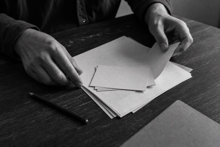 Hands arranging blank cards and paper on a dark wooden table.